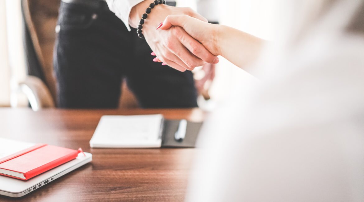Aperto de mãos entre profissionais em escritório, representando acordo e compliance empresarial