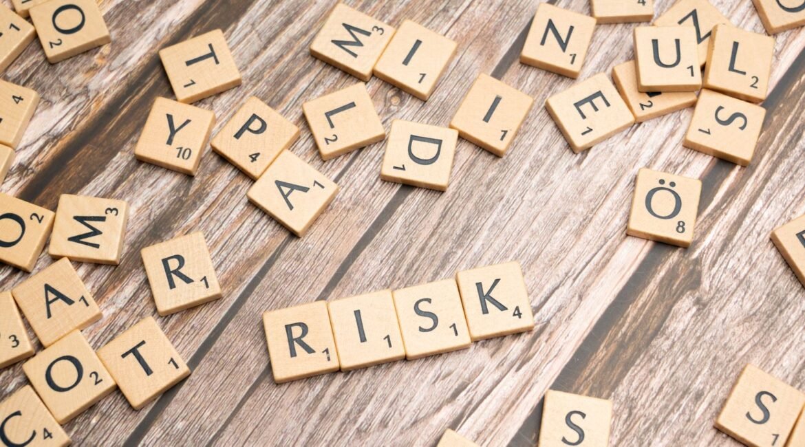 Peças de Scrabble formando a palavra RISK (risco) sobre uma mesa de madeira